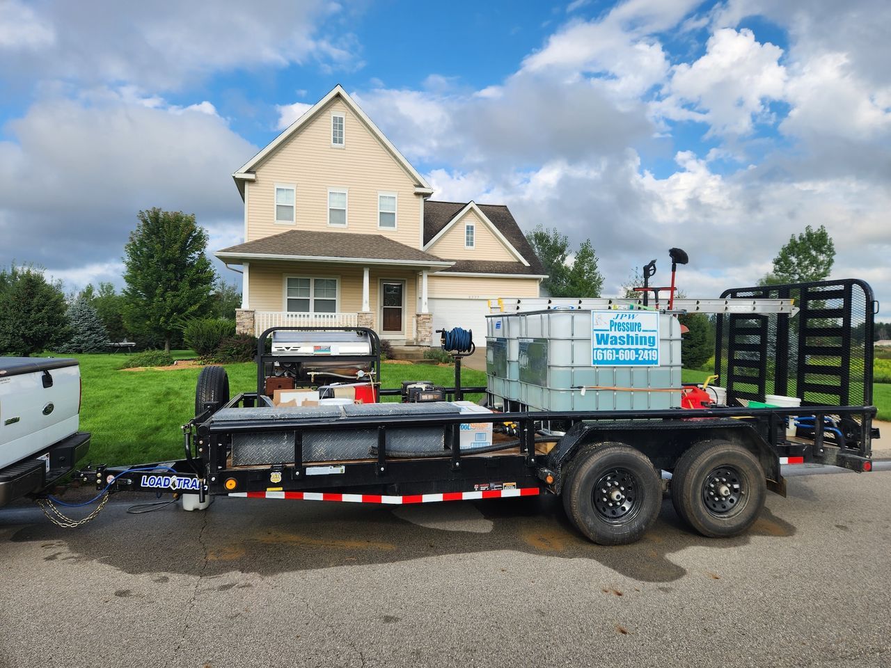 A trailer with equipment parked on a street in front of a house on a sunny day.