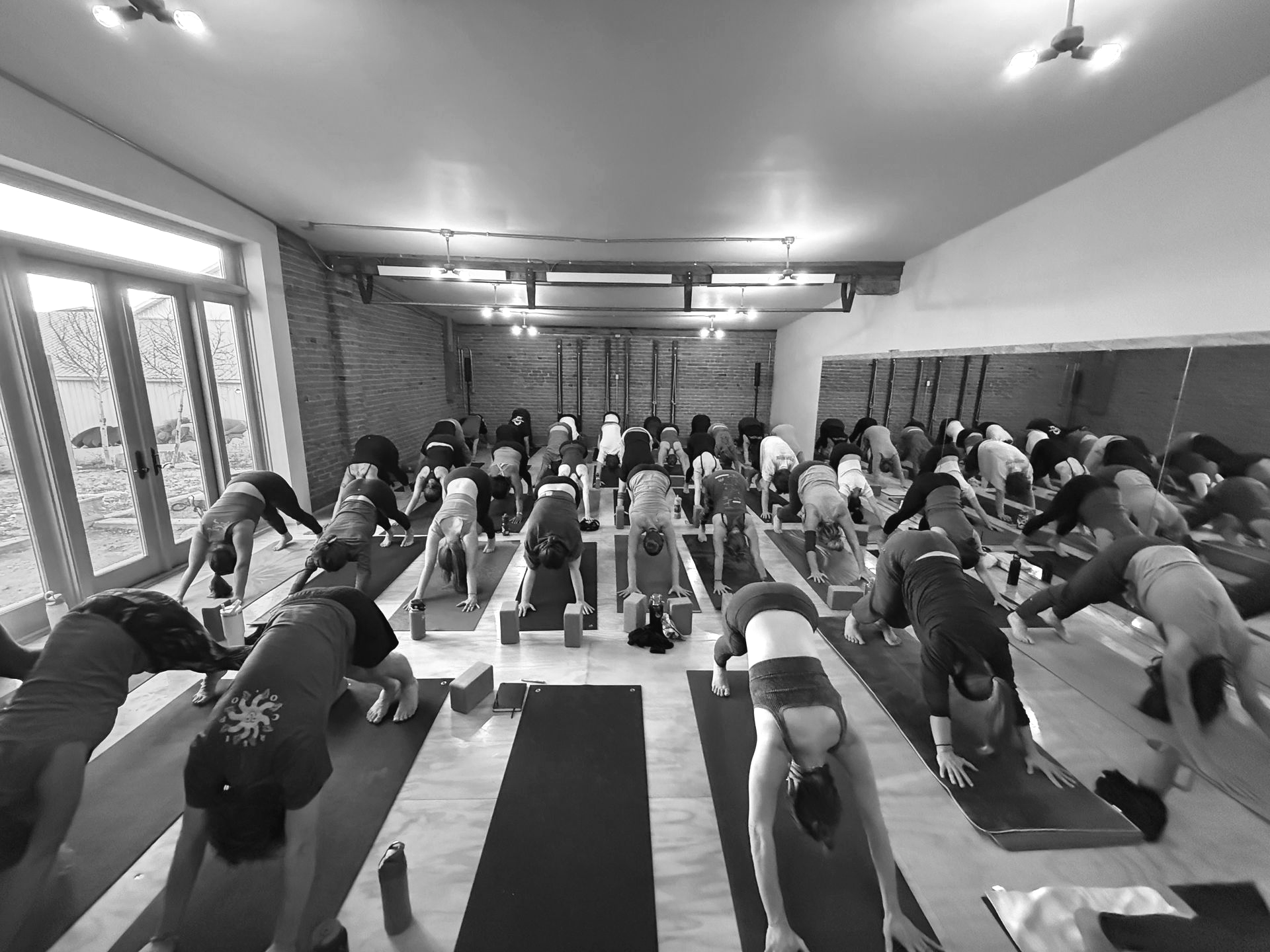 Woman in downward-facing dog pose with one leg extended upwards, on yoga mat. Black and white photo.