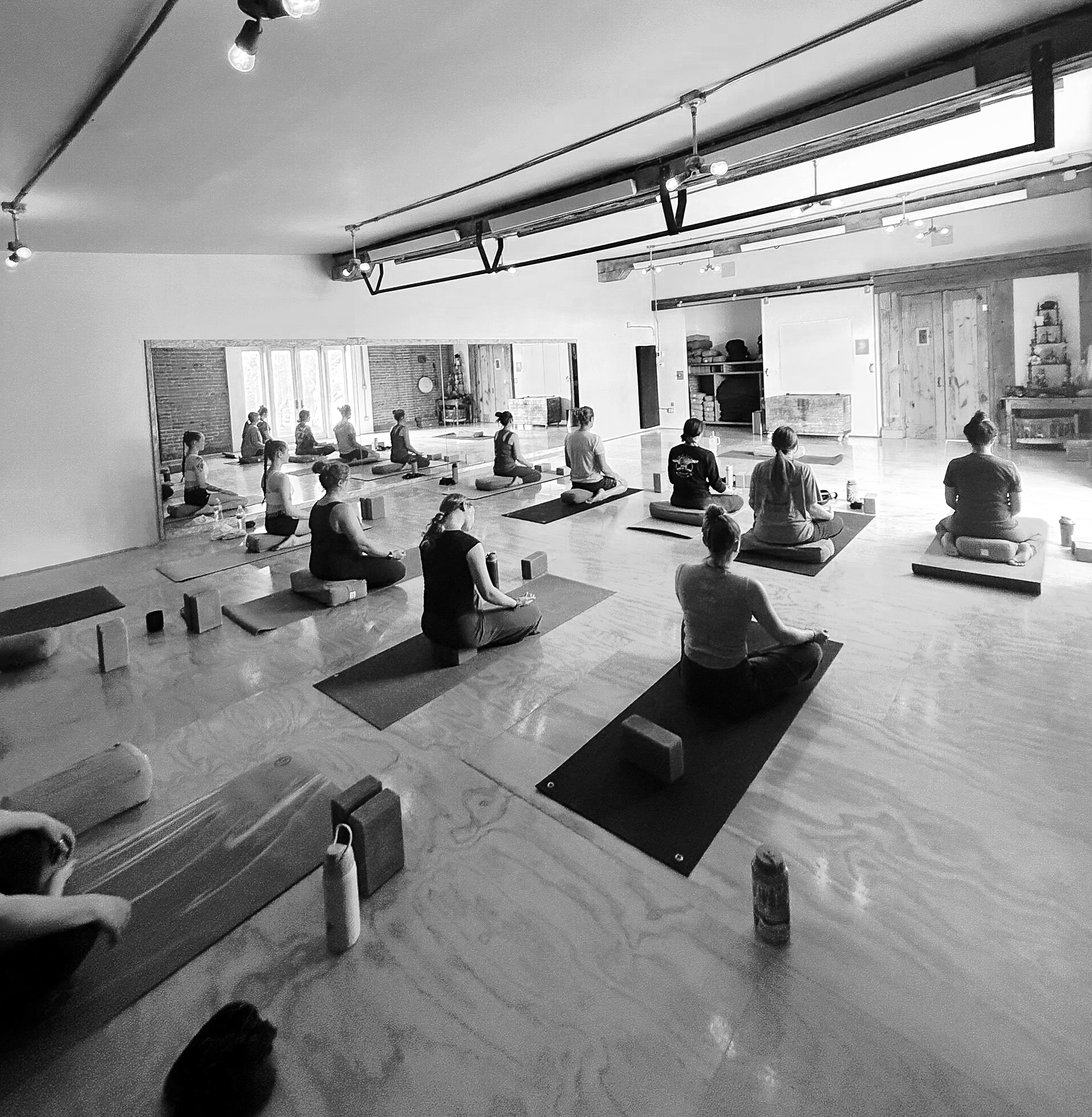 People in yoga class, reaching towards floor. Stacked blanket, block, and strap in foreground.