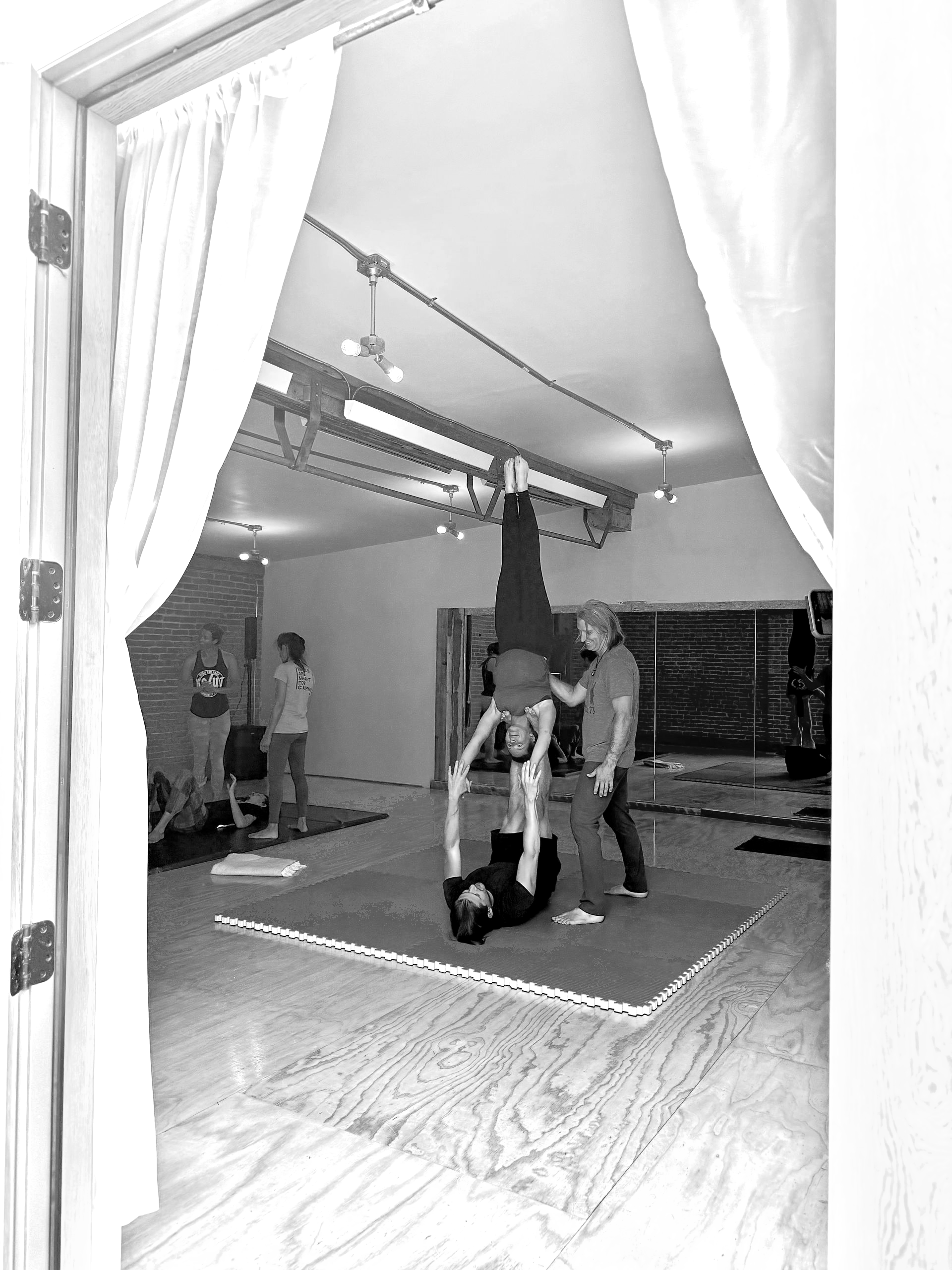 Woman in black athletic wear doing yoga pose with one foot on a chair, reaching arm overhead.