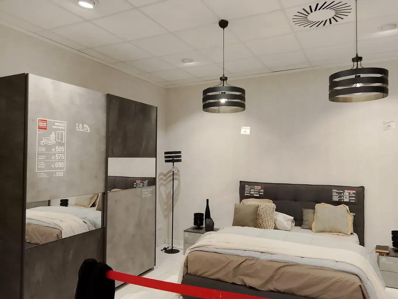 Camera da letto moderna con due letti, lampade a sospensione nere e armadio con ante a specchio.
