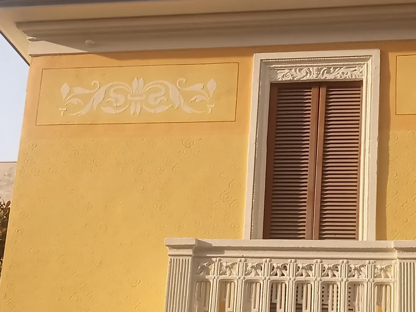 Facciata gialla dell'edificio con balcone bianco e finestra con persiane marroni.
