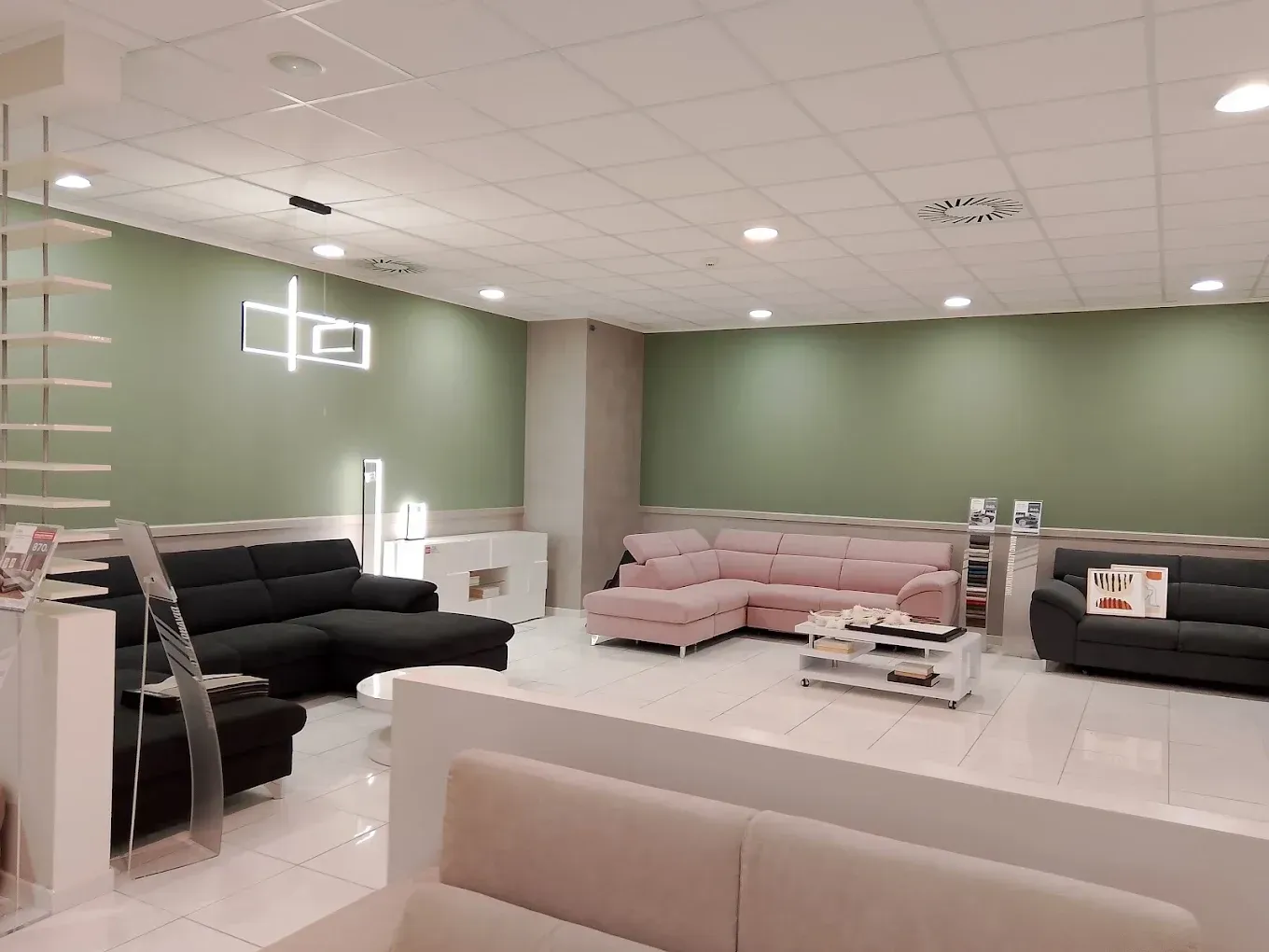 Showroom di mobili moderni con divani, pavimento bianco lucido, parete d'accento verde e luci a soffitto.