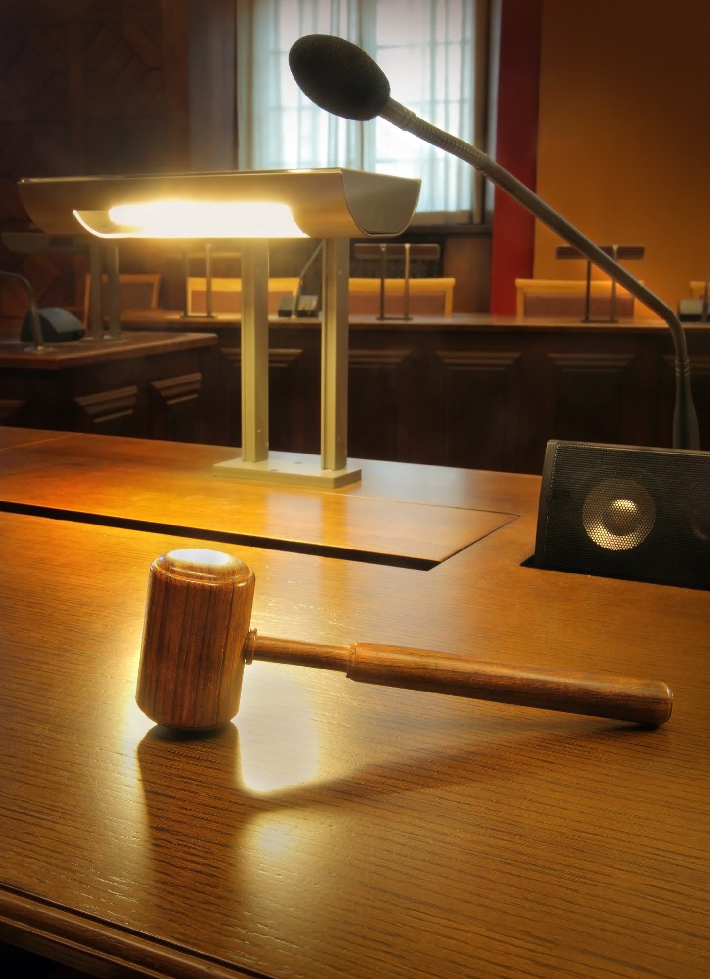 Wooden gavel on a shiny table in a courtroom, with a microphone and lamp.