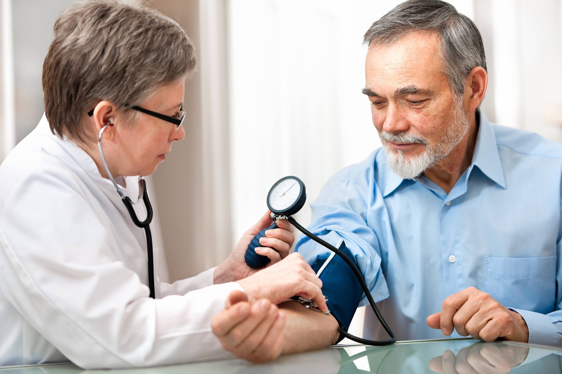 Doctor taking a patient's blood pressure. Blue cuff on arm, stethoscope, man looking down.