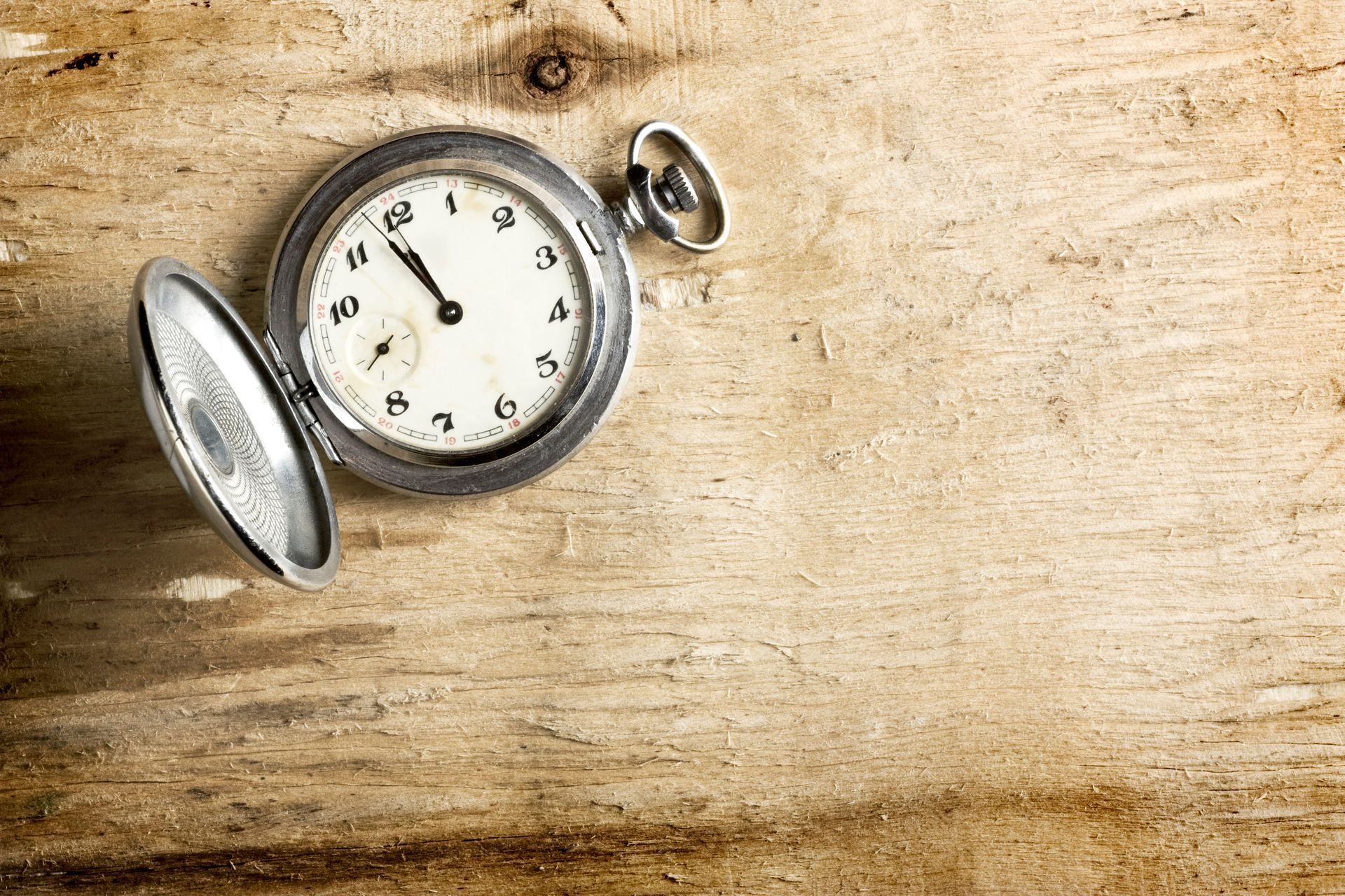Pocket watch on wooden surface, showing time as five minutes before 11.