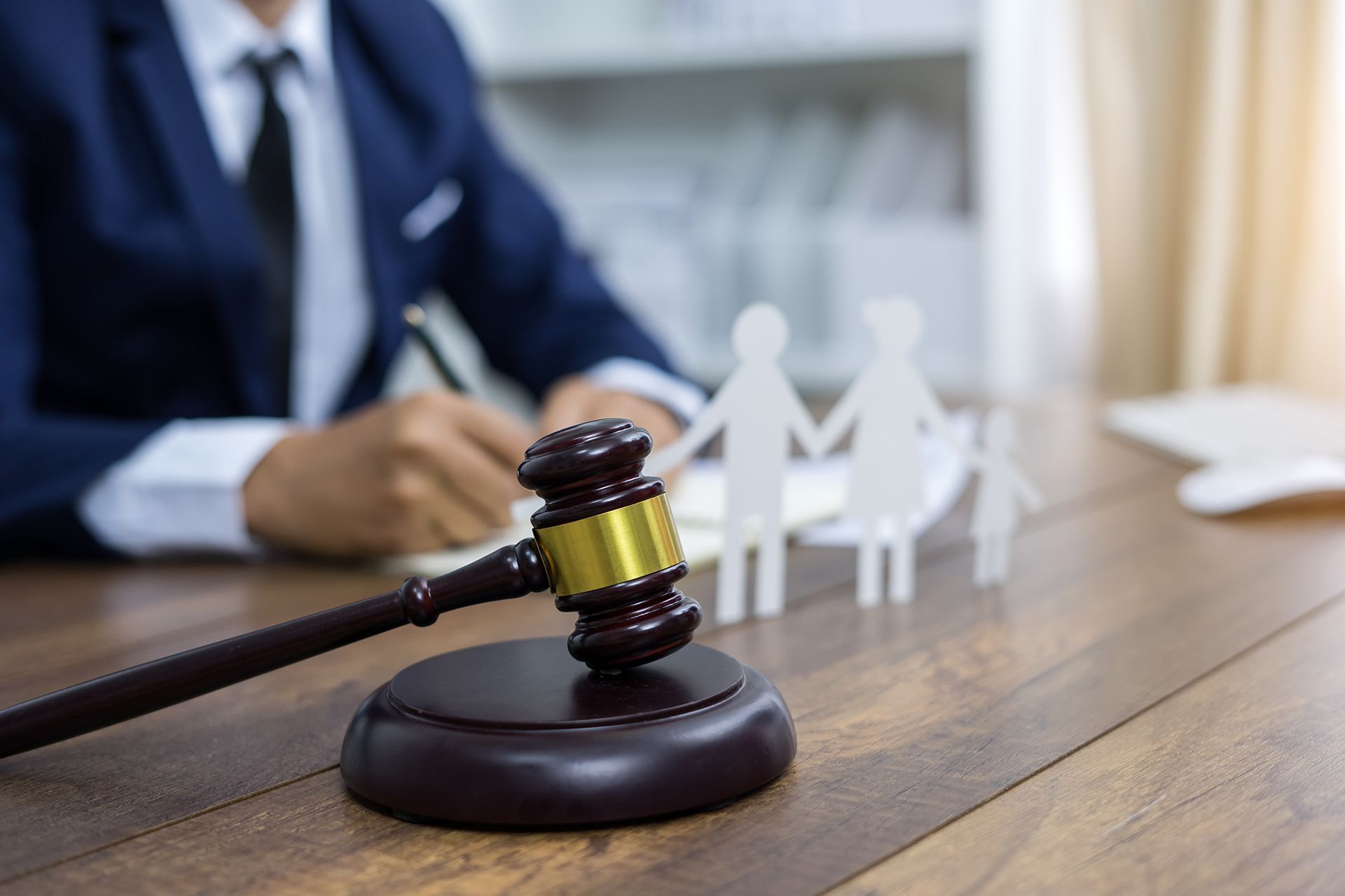 Gavel on wooden desk with family cutouts; a person in a suit writes in the background.