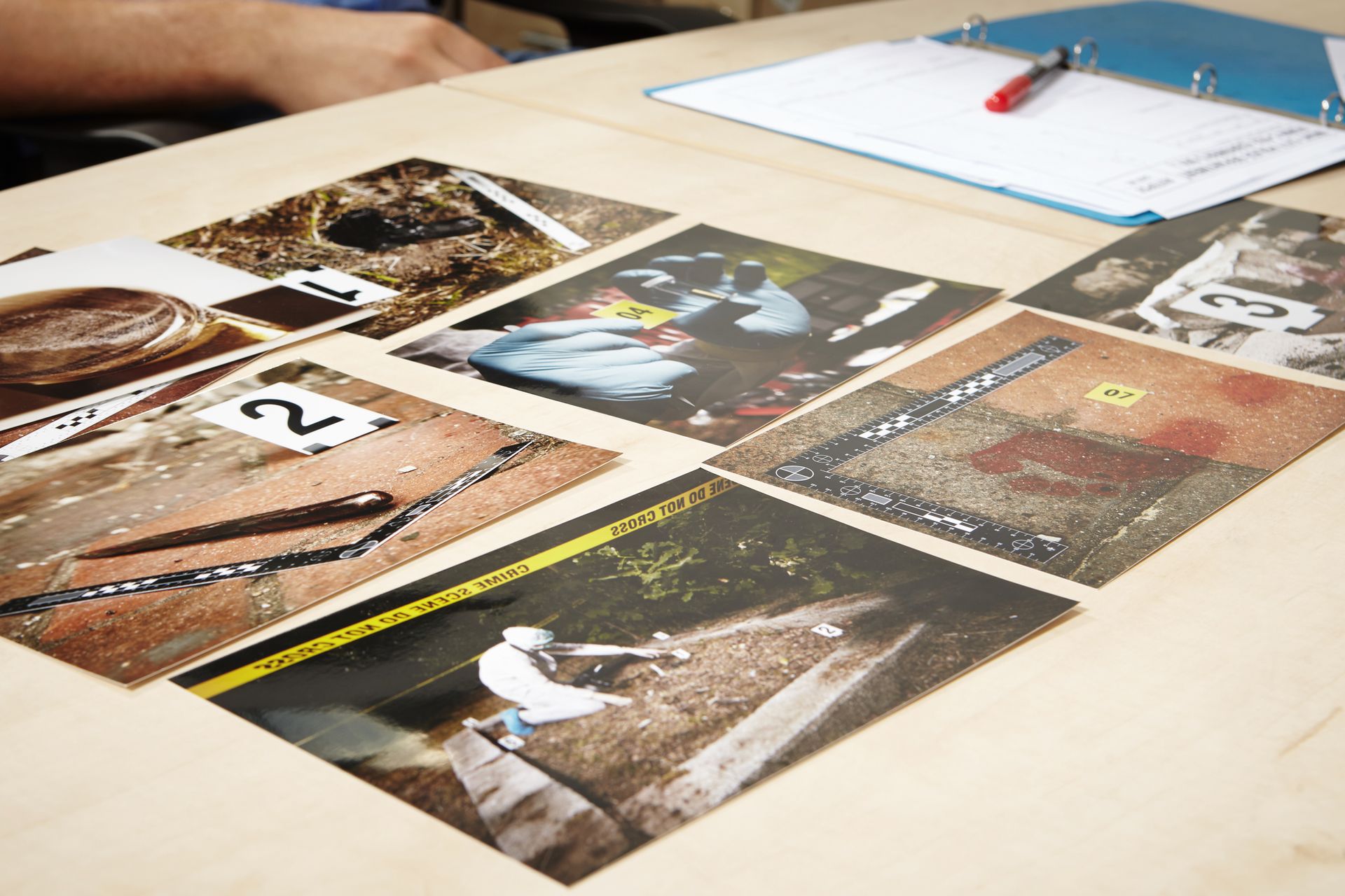 Photos of a crime scene laid out on a table for examination, with a pen and notepad visible.