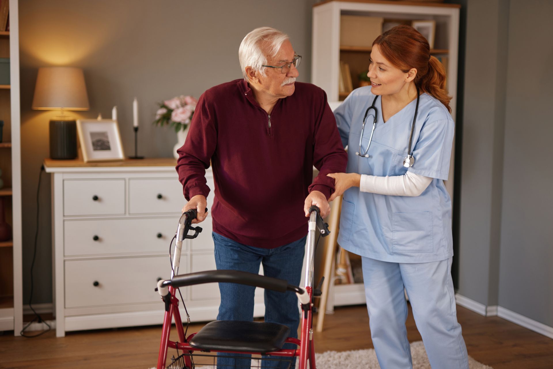A nurse wearing scrubs helps an elderly man.