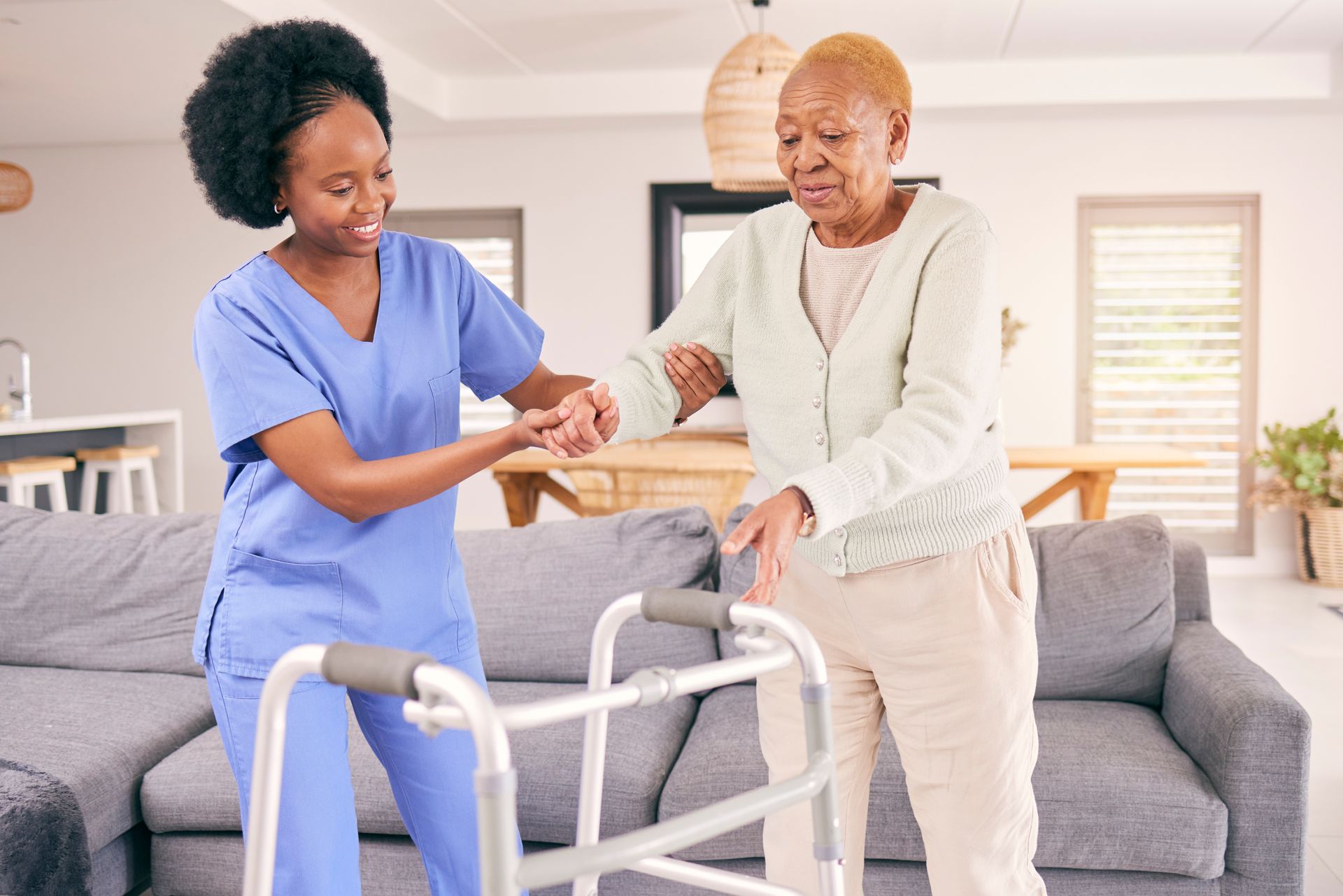 A nurse assists an elderly woman using a walker, providing support and guidance at home.