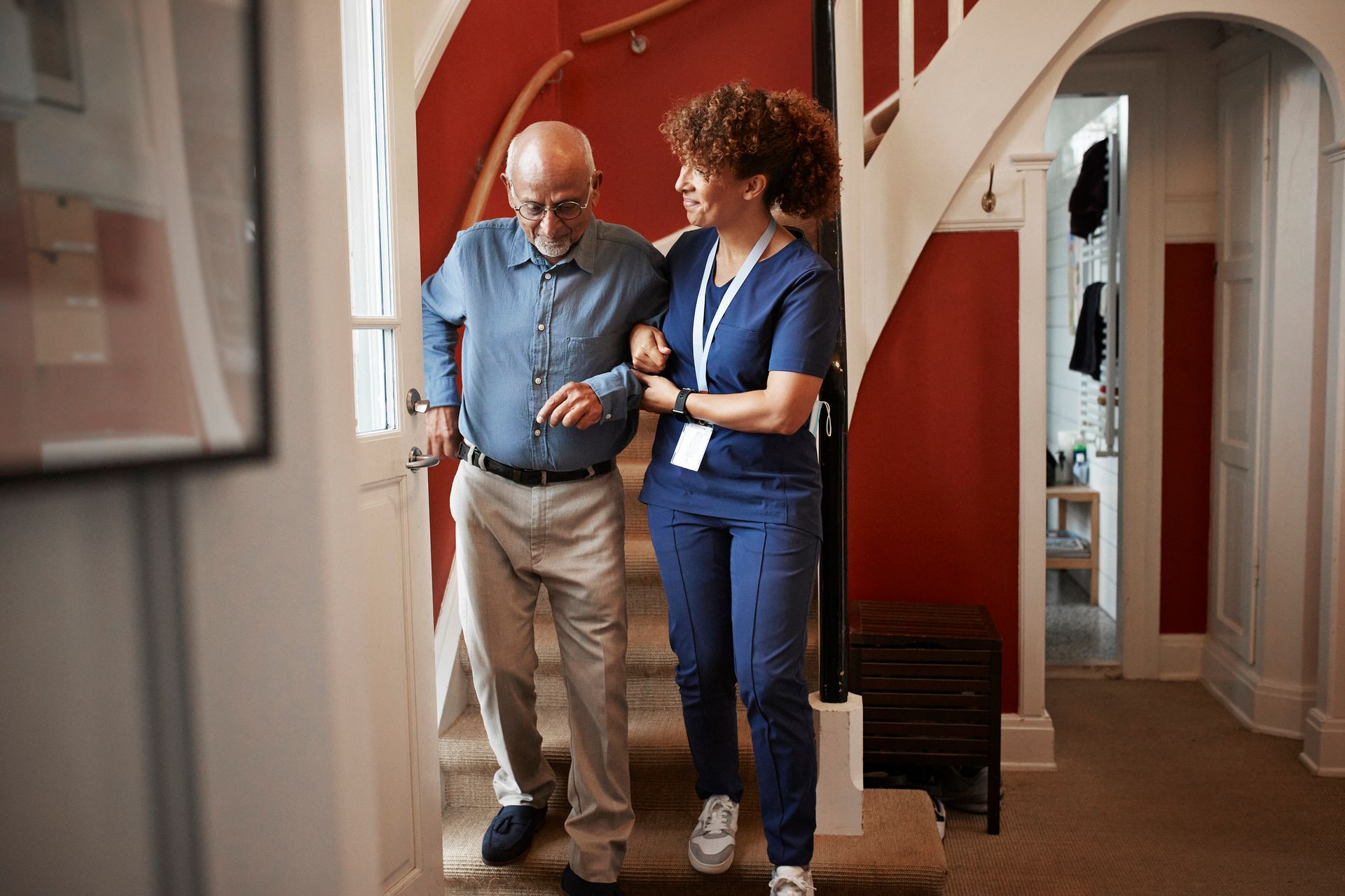 Elderly person assisted by caregiver walking downstairs at home.