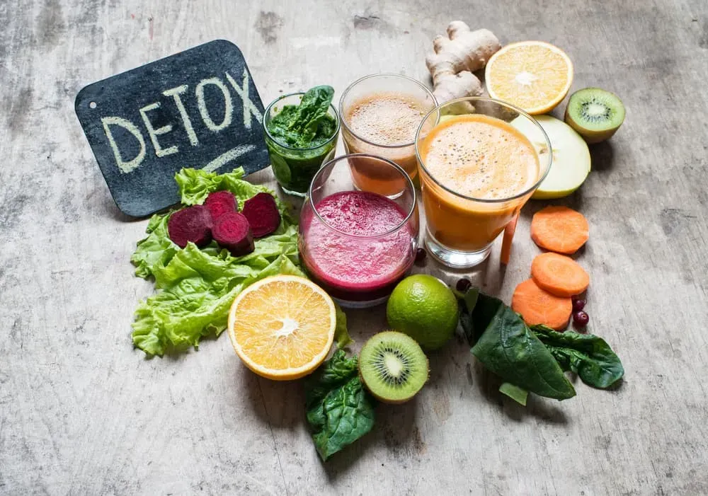 Detox smoothie ingredients with fruits, vegetables, and two colorful blended drinks on a rustic table.