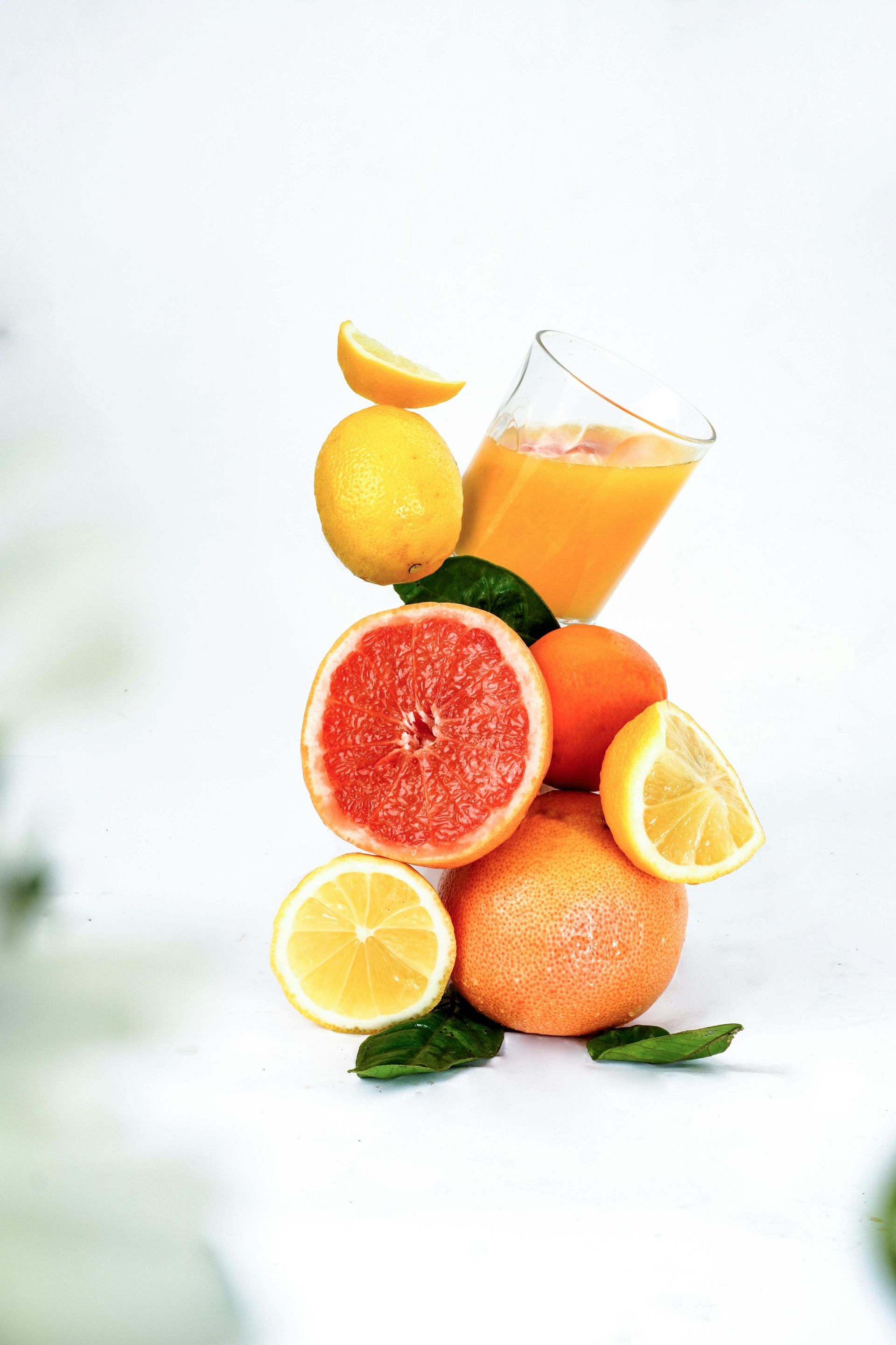 Citrus fruits stacked with a glass of orange juice on a white background.