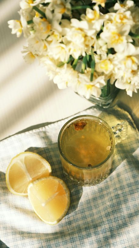 Yellow citrus halves beside a glass of tea on a plaid cloth, with white flowers in the background.