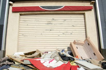 Roller shuttered storefront with awning, debris piled in front.