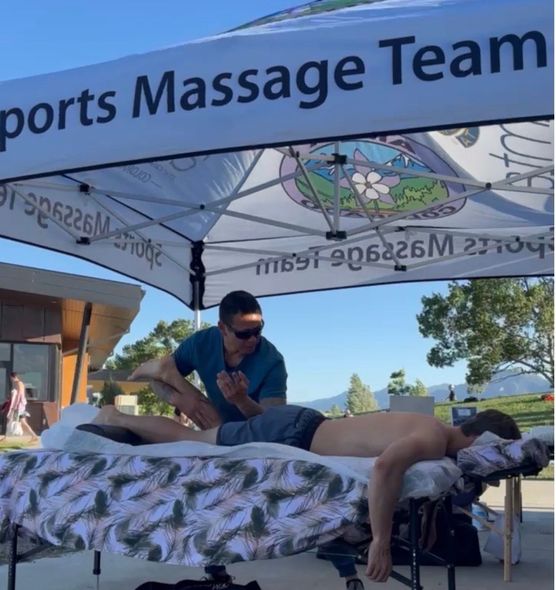 Tim performing outdoor manual therapy under a Sports Massage Team tent with mountains behind