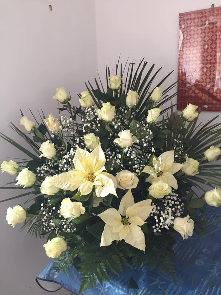 Composizione floreale con rose bianche e stelle di Natale, su un tavolo apparecchiato di blu.