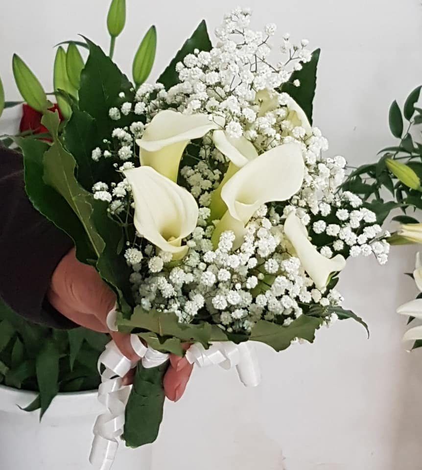 Primo piano di una mano che regge un piccolo bouquet di calle bianche e gypsophila, legato con un nastro bianco.