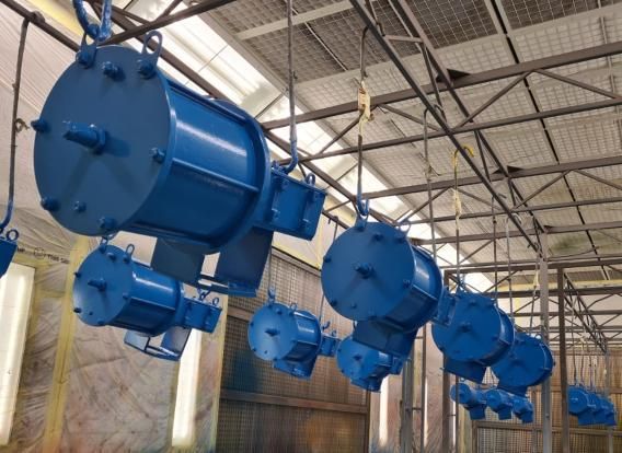 Macchinari industriali blu appesi a scaffalature sospese in una fabbrica.