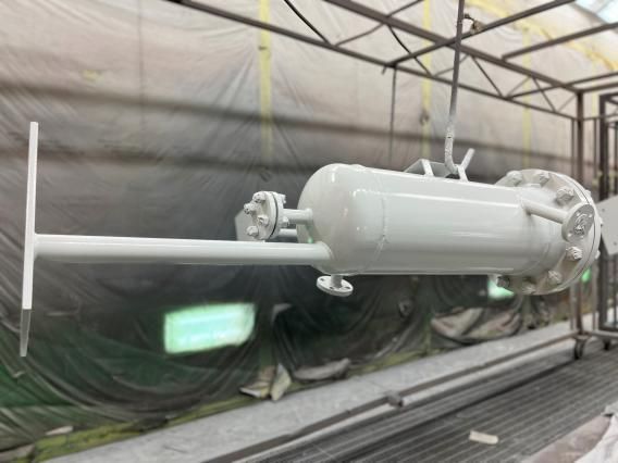 Serbatoio industriale verniciato di bianco sospeso in una cabina di verniciatura.