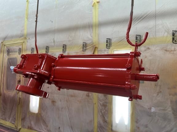 Attuatore industriale verniciato di rosso appeso in una cabina di verniciatura.