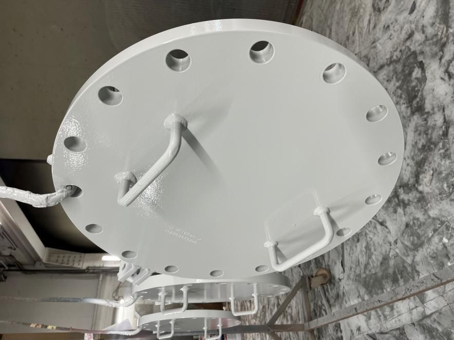 Grande coperchio rotondo in metallo bianco con fori per bulloni e maniglie. Ambiente industriale.