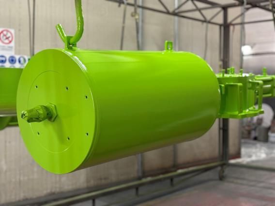 Componente industriale cilindrico di colore verde brillante appeso a un gancio.