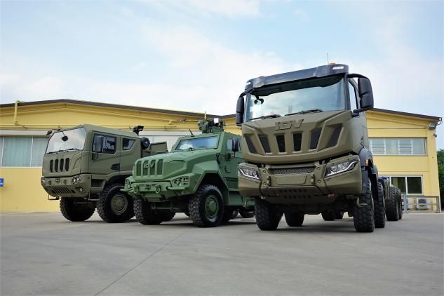 Tre camion militari verde oliva parcheggiati davanti a un edificio.