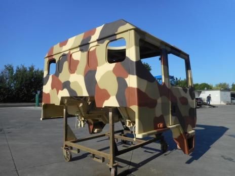 Cabina di camion dipinta con vernice mimetica su supporto con ruote, all'aperto. Include motivi marroni, beige e grigi.