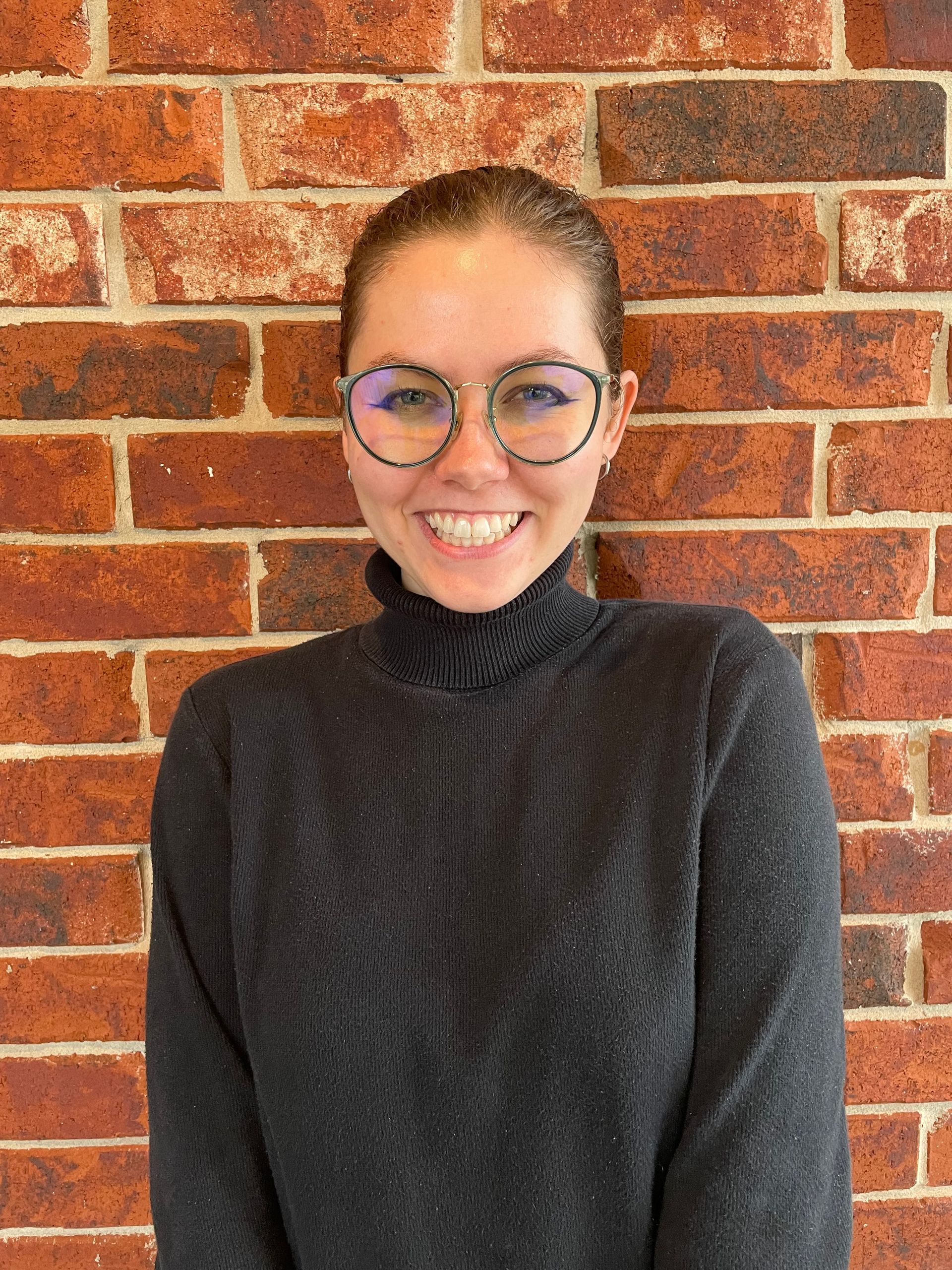 A woman in a red plaid shirt is smiling in front of a brick wall.