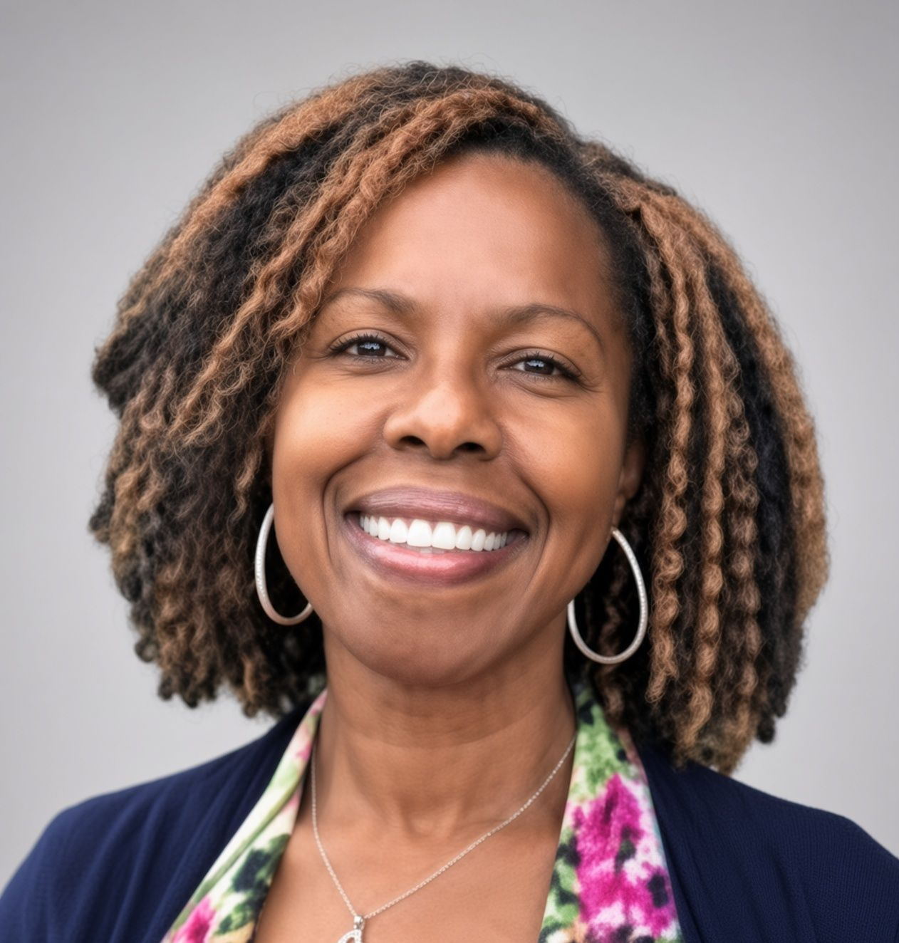 A woman with dreadlocks is smiling for the camera in front of a bush.