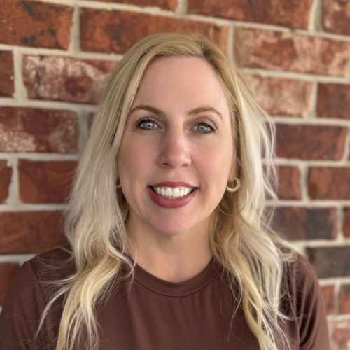A woman in a red plaid shirt is smiling in front of a brick wall. A woman in a red plaid shirt is smiling in front of a brick wall.