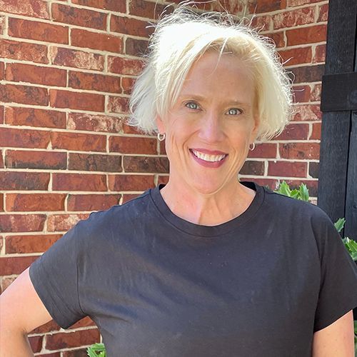 A woman in a black shirt is smiling in front of a brick wall.