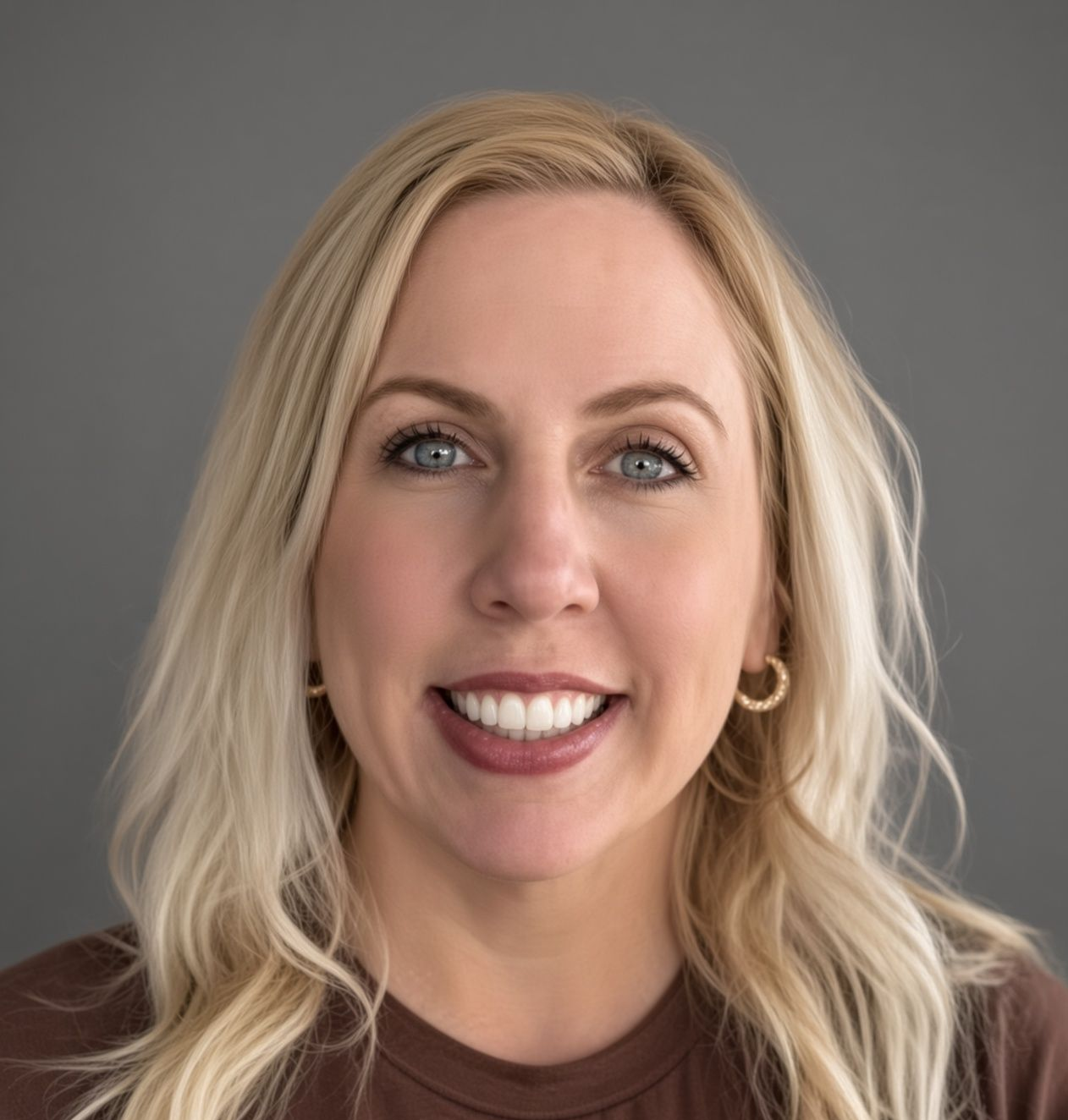 A woman is smiling in front of a brick wall.