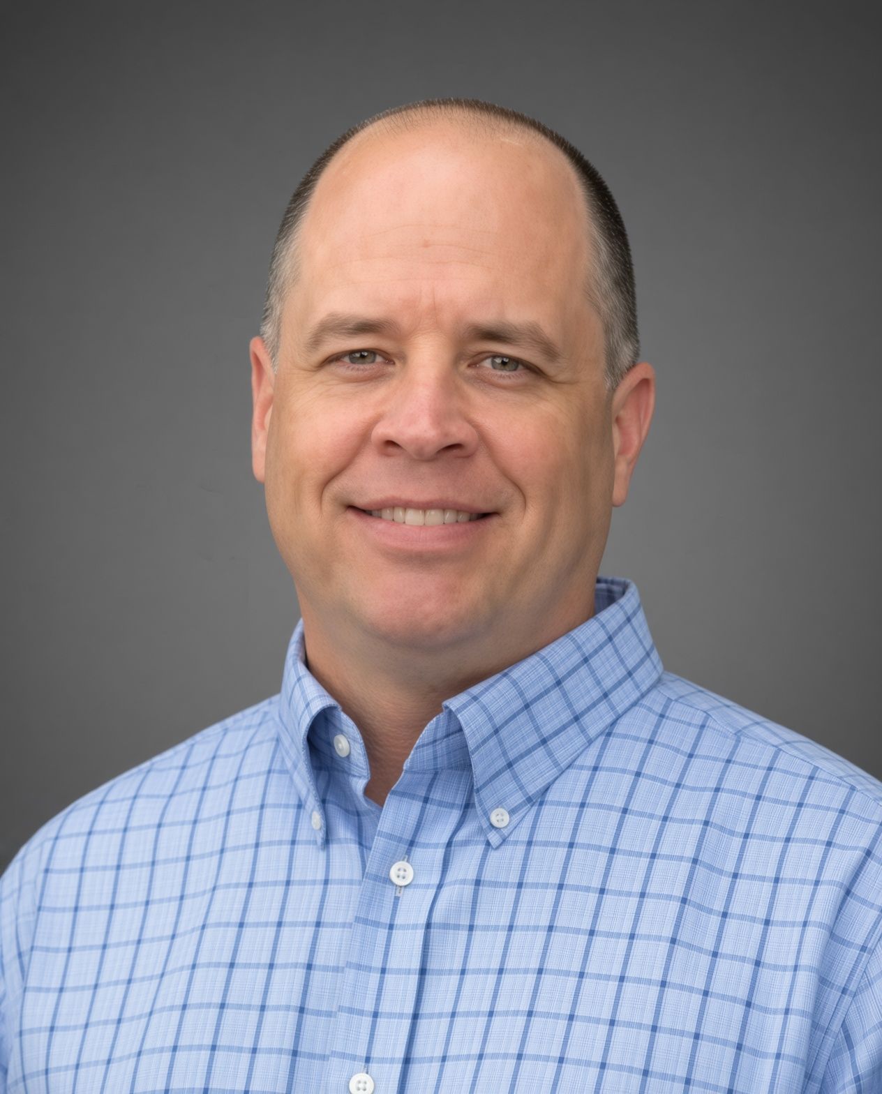 A man in a blue plaid shirt is standing in front of a bush.