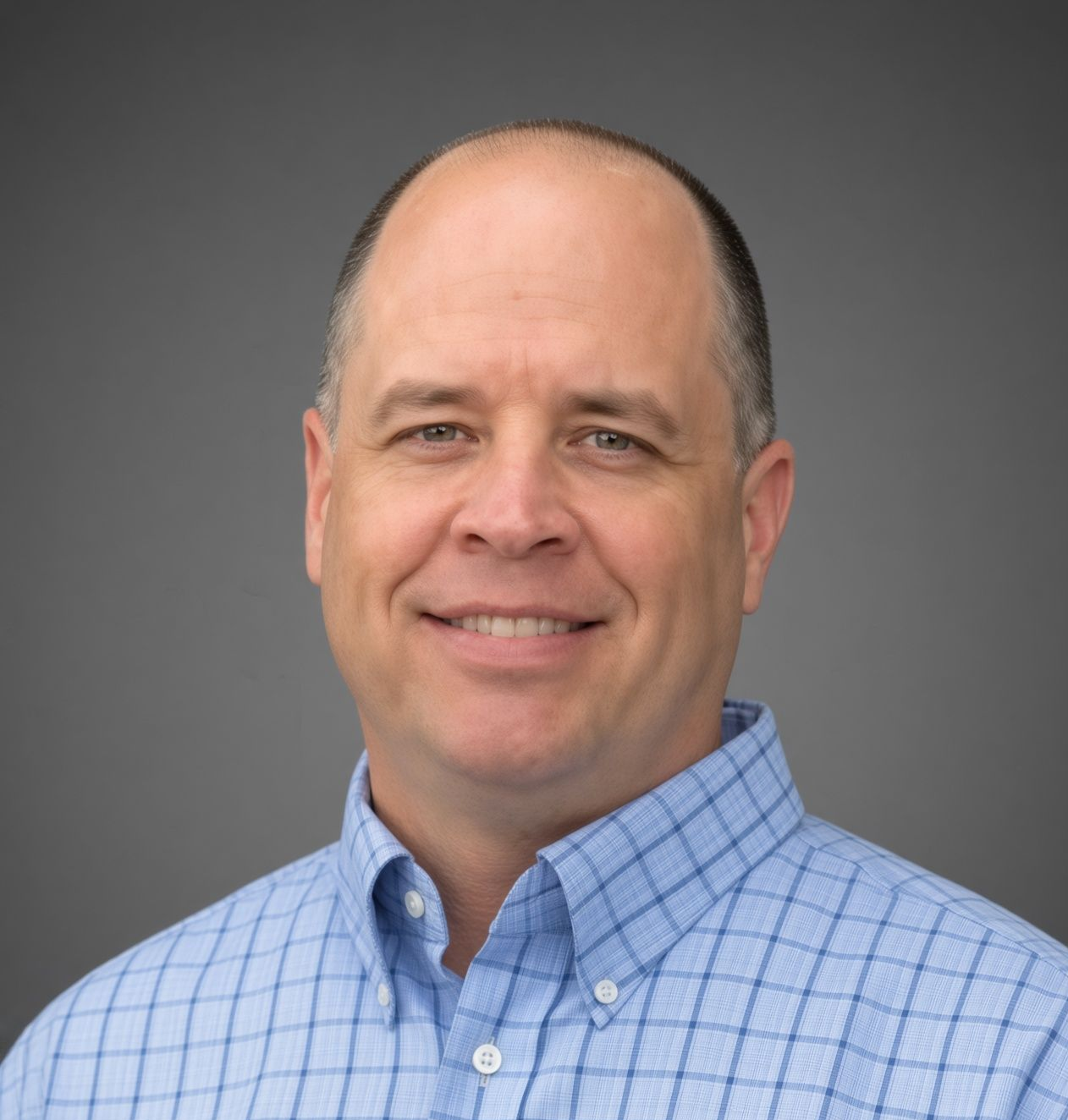 A man in a blue plaid shirt is standing in front of a bush.