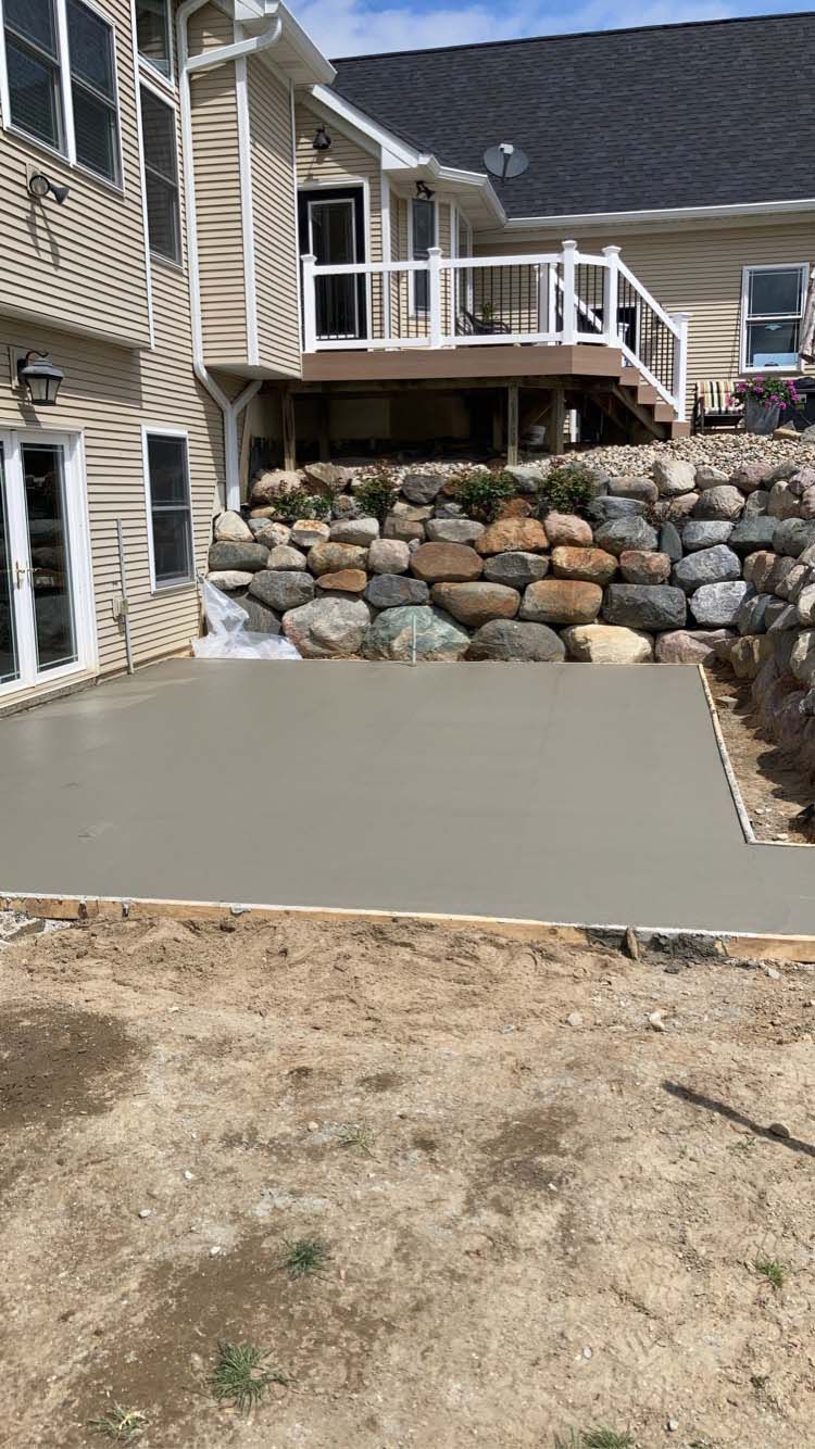 Newly poured concrete patio next to a house with a rock retaining wall.