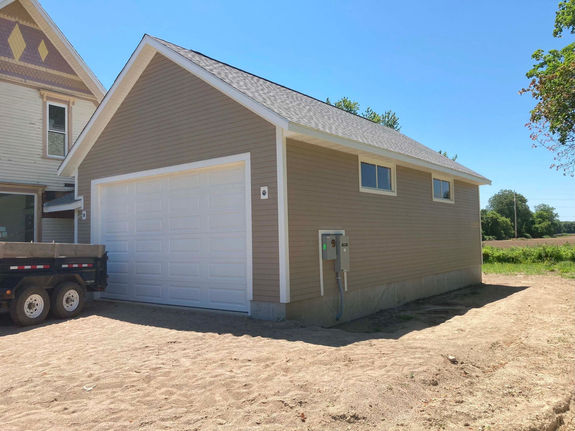 Tan garage next to house, white door, windows. Dirt lot, blue sky.