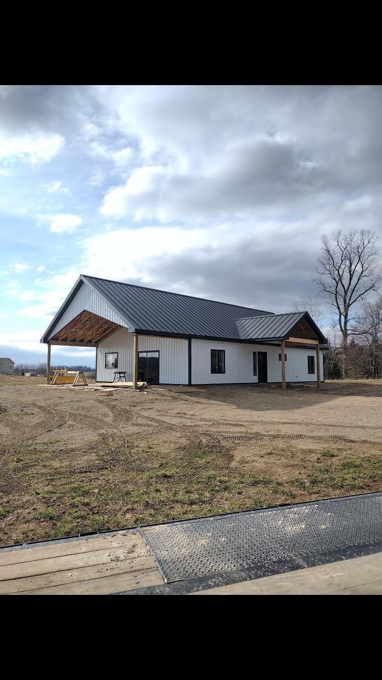 White and black building with a metal roof on a grassy field under a cloudy sky.