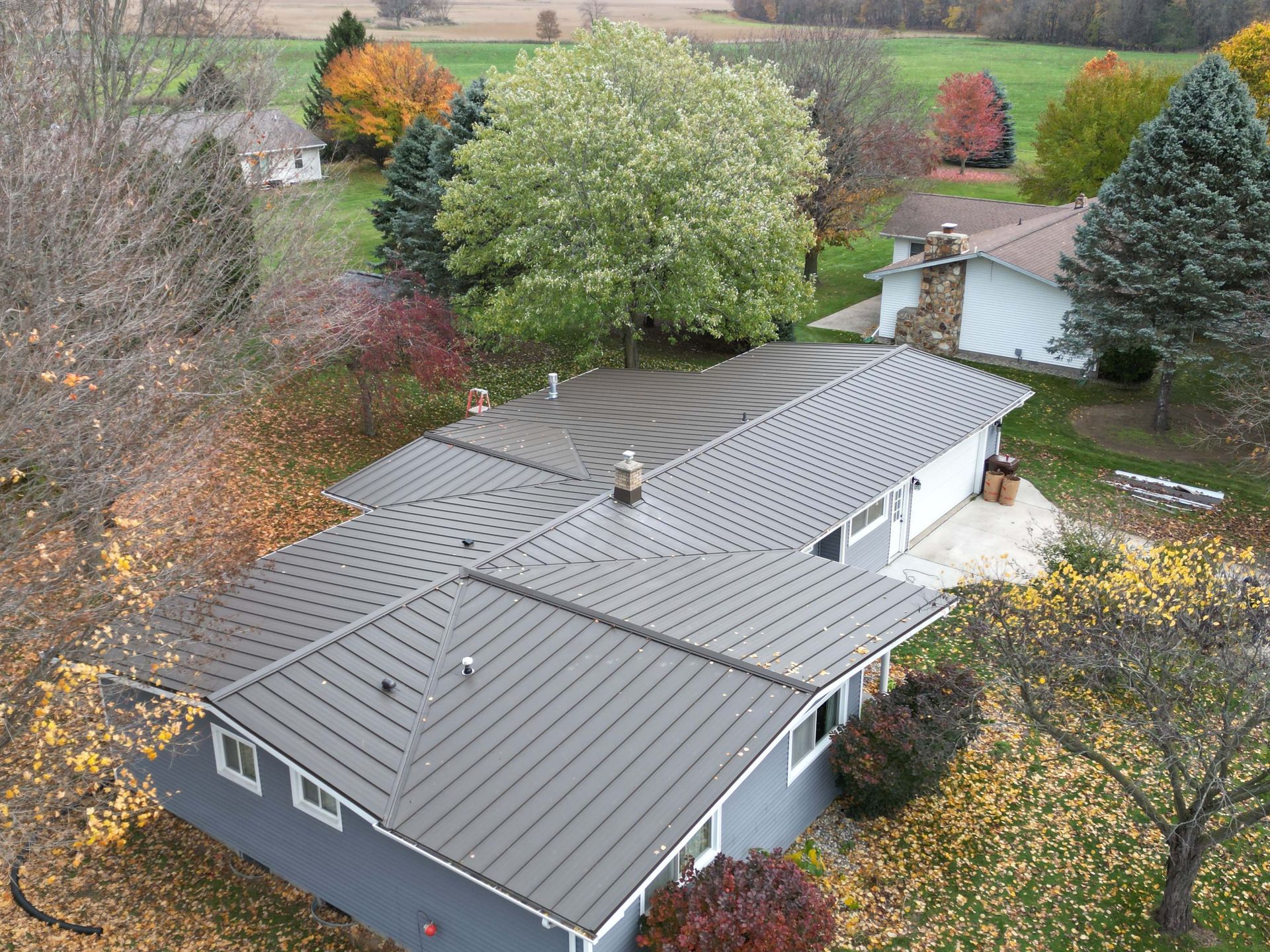 Gray metal roof of a house, surrounded by trees with fall foliage.