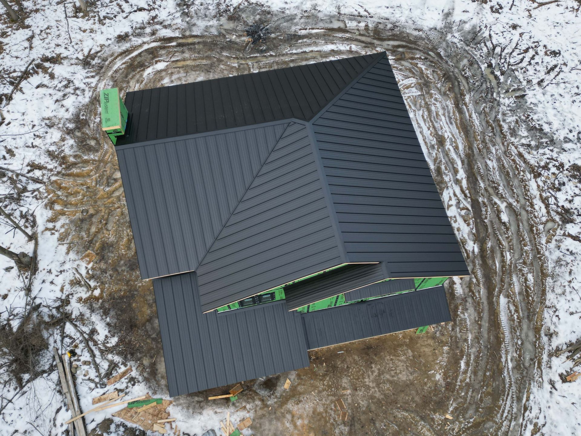 Aerial view of a dark roof house under construction, surrounded by snow and dirt.