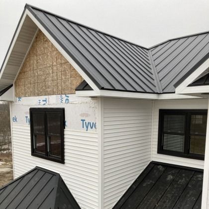 White house with black metal roof, windows, and trim.