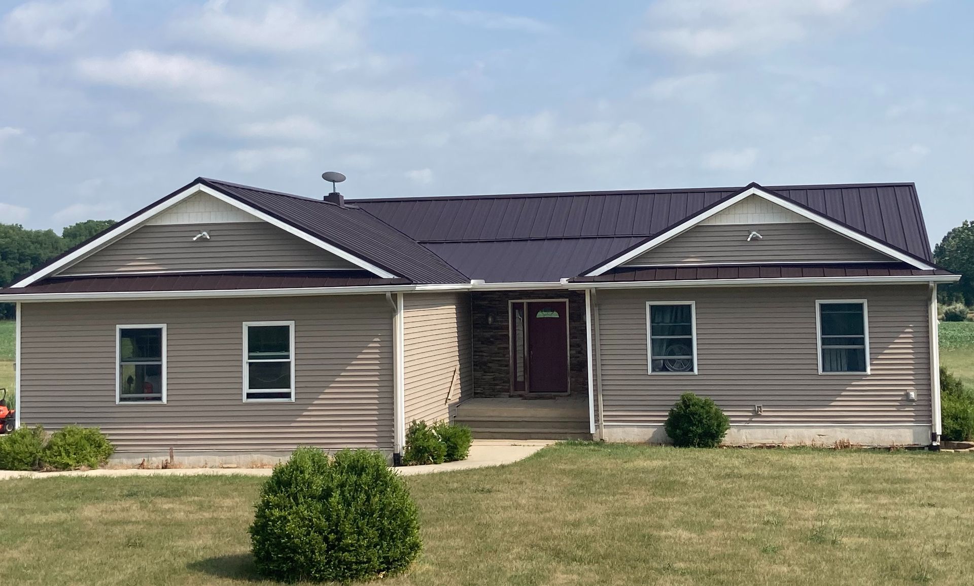 Tan ranch-style home with a dark purple roof and siding, set against a field under a cloudy sky.