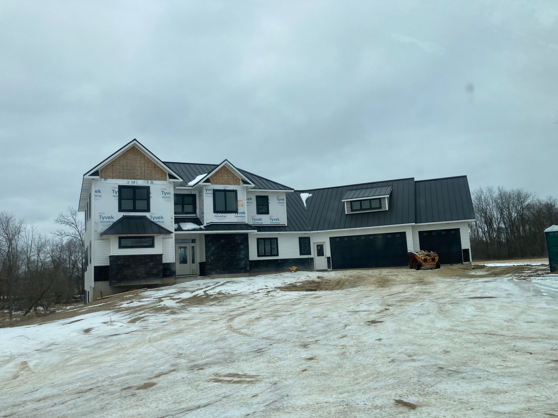 New two-story house under construction on a snowy hill, with black roof, windows, and garage doors.
