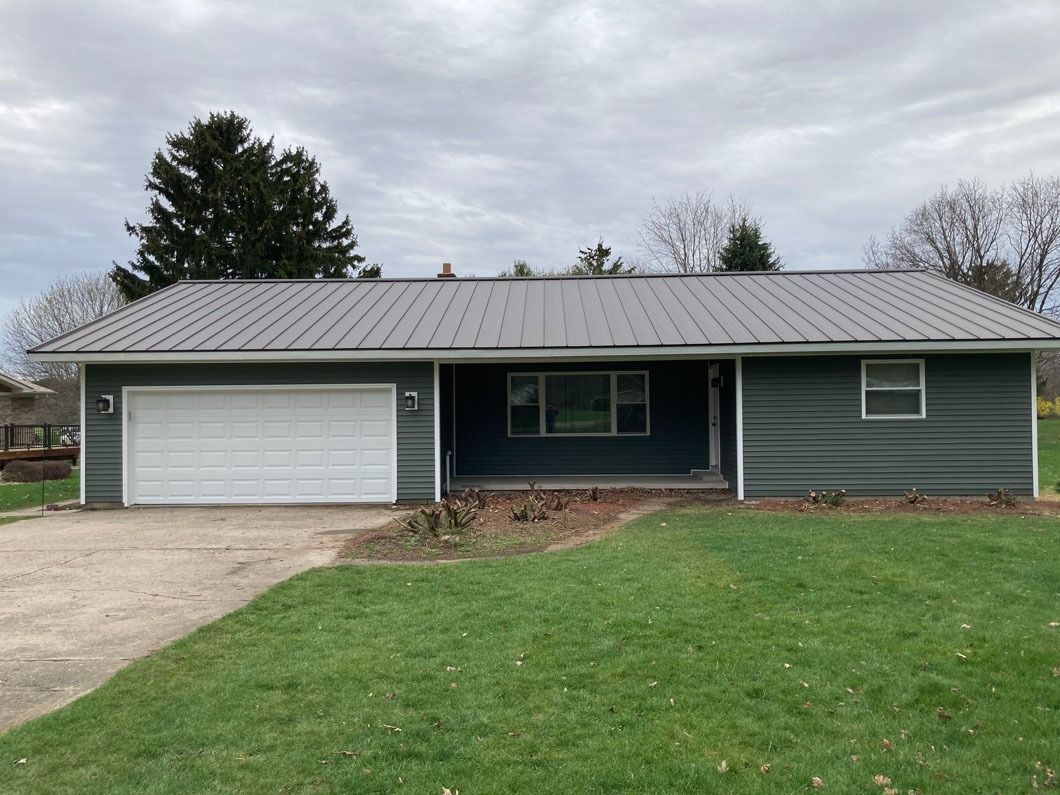 Green house with gray metal roof and white garage door on a cloudy day.