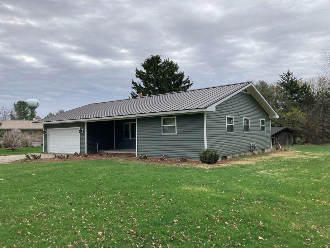 A single-story blue house with a gray roof and attached garage, set on a green lawn.