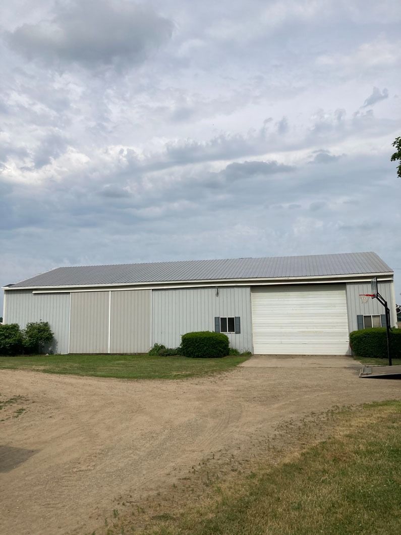 Large white barn with a large garage door, under a cloudy sky.