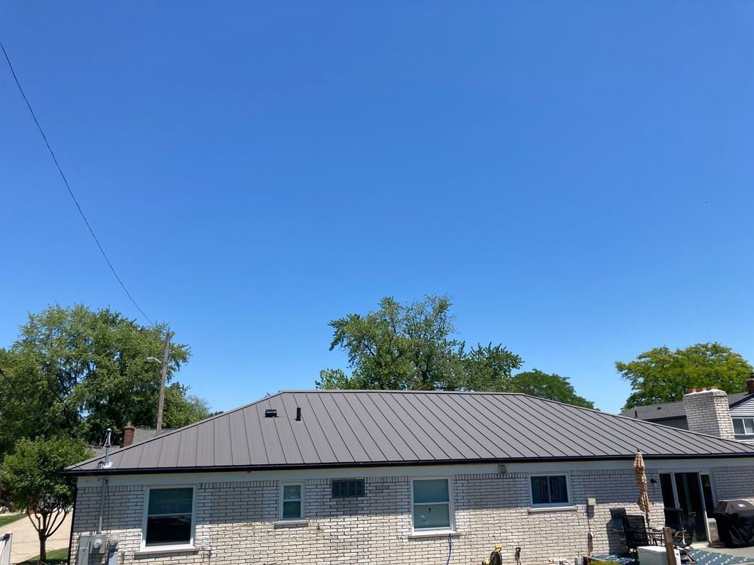 A gray-roofed house with windows, surrounded by trees, under a clear blue sky.