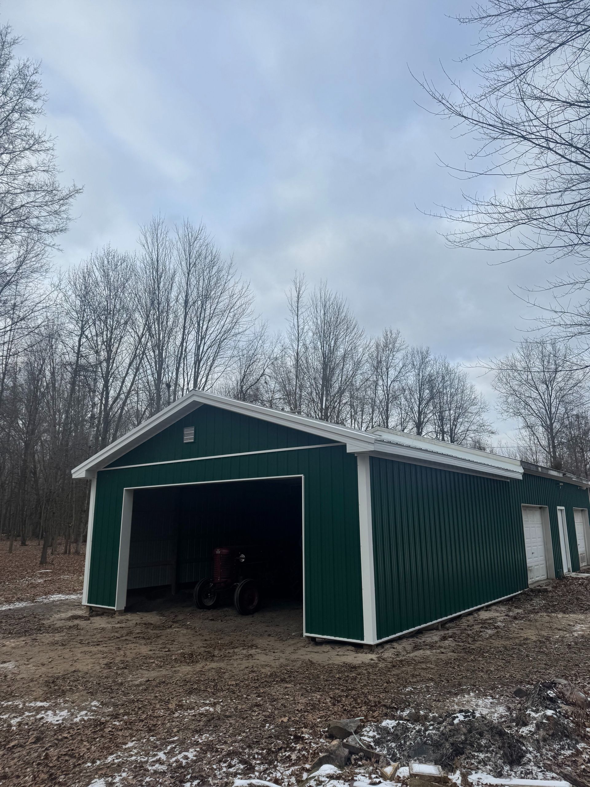 Green metal shed with open bay, set in a winter landscape with bare trees and a cloudy sky.
