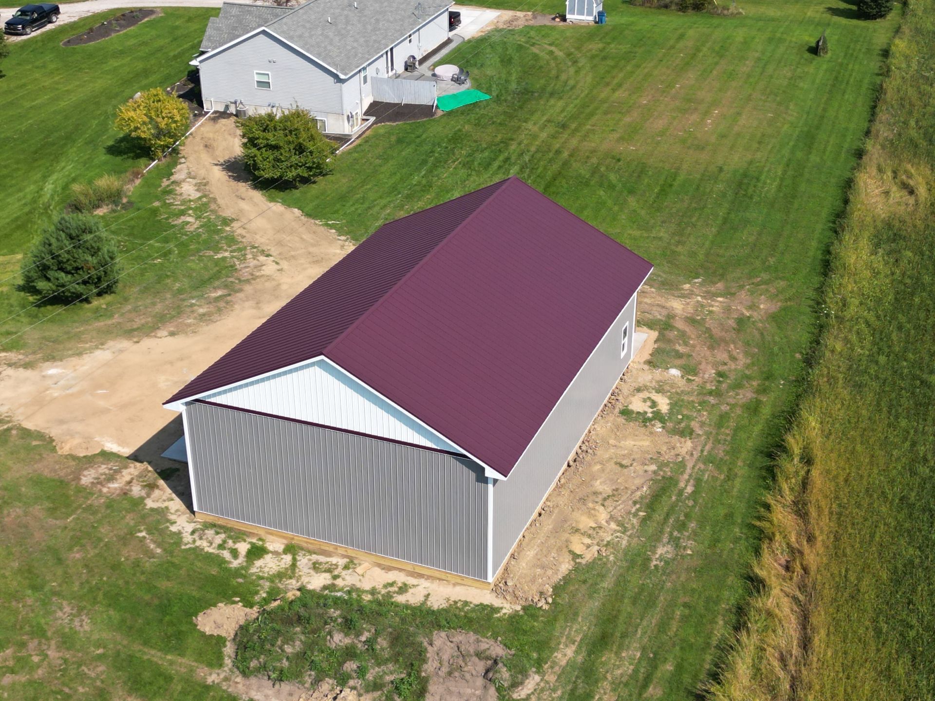 A metal-roofed gray building with white trim, set in a grassy yard, near another house.